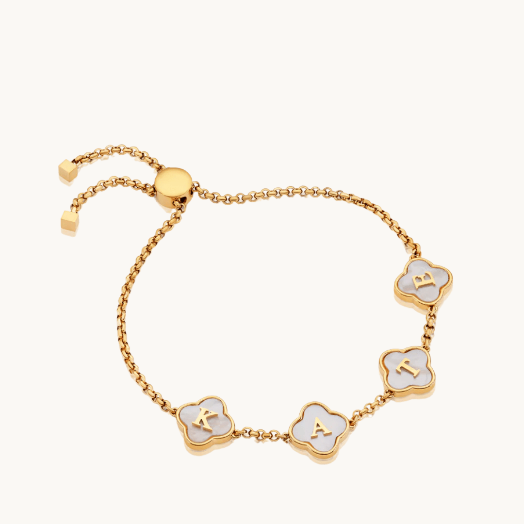 gold-plated clover bracelet with white pearls and engraved initials on flat lay