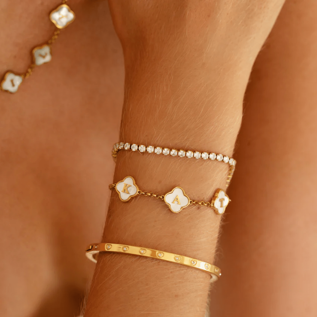 elegant clover bracelet with heart charm and initials worn on tanned wrist